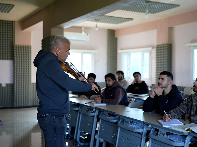 A music lecturer playing the violin for students in class